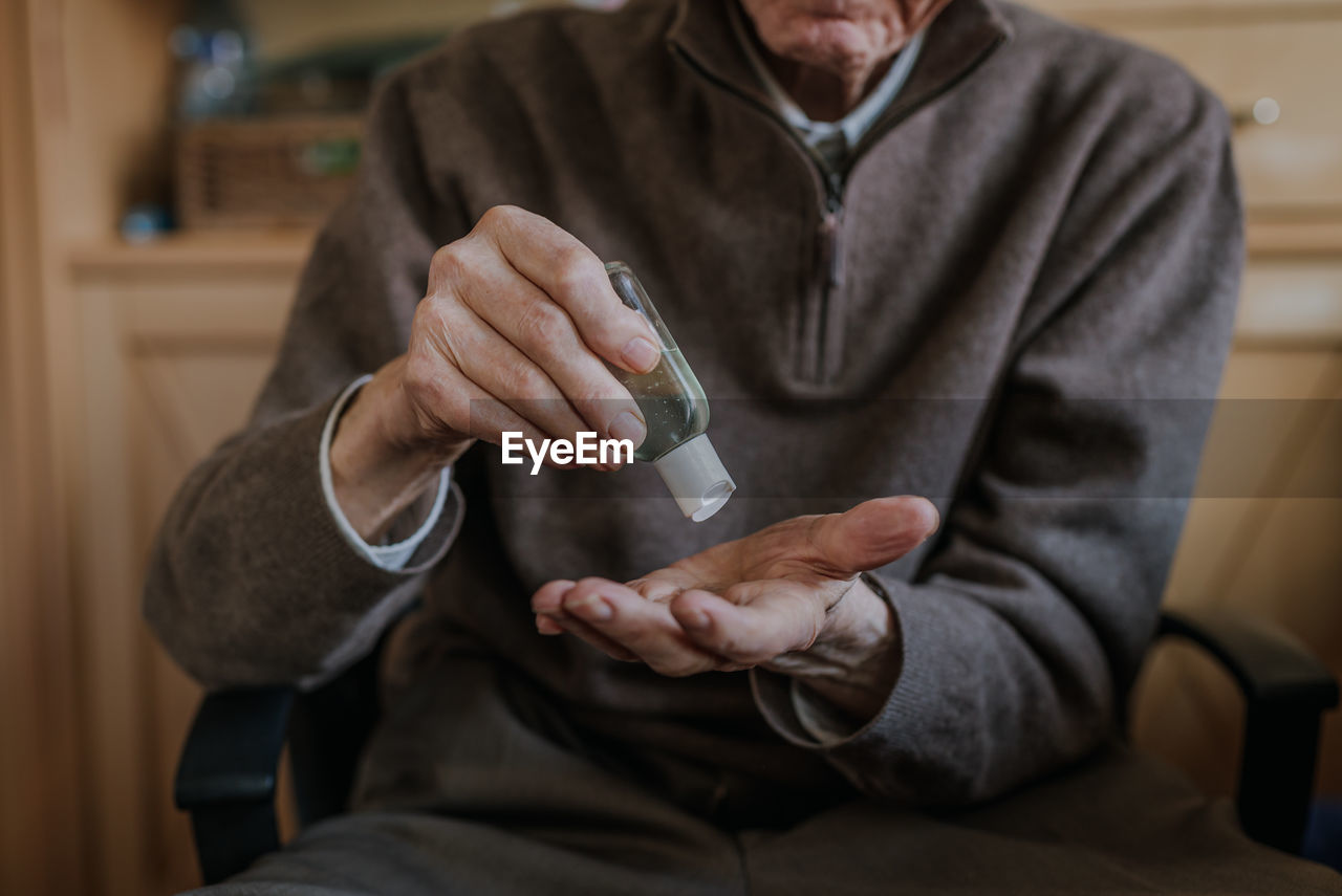 Midsection of senior man using hand sanitizer at home
