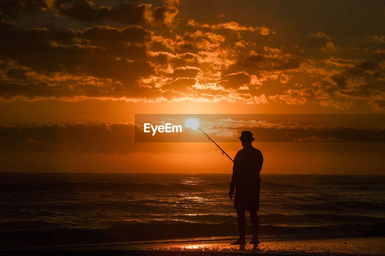 Silhouette man fishing at beach against sky during sunset