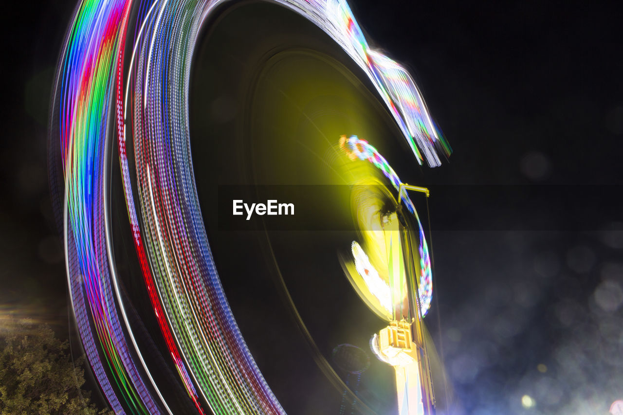 Low angle view of illuminated ferris wheel spinning at night