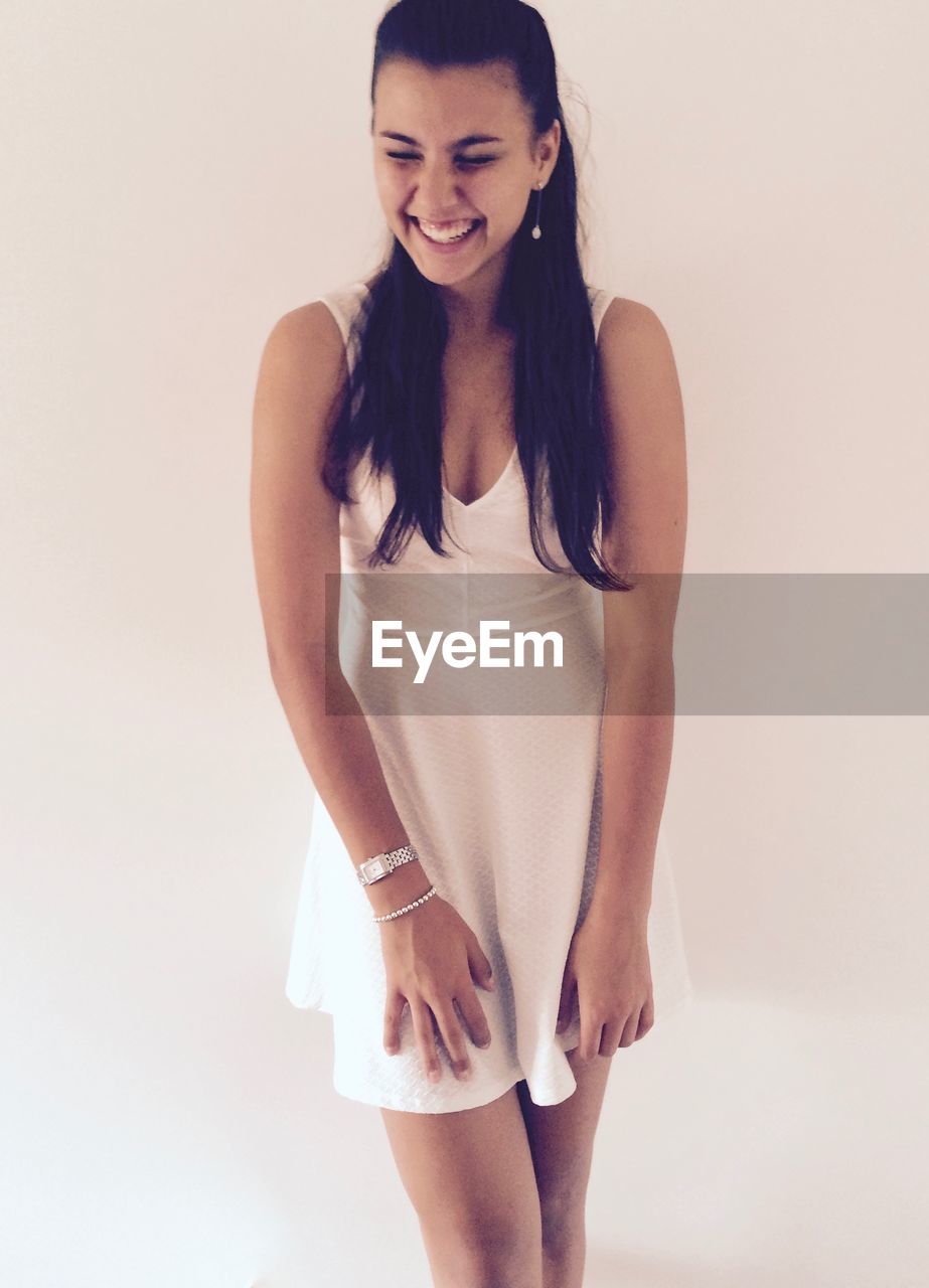 Smiling woman in white dress standing against white background