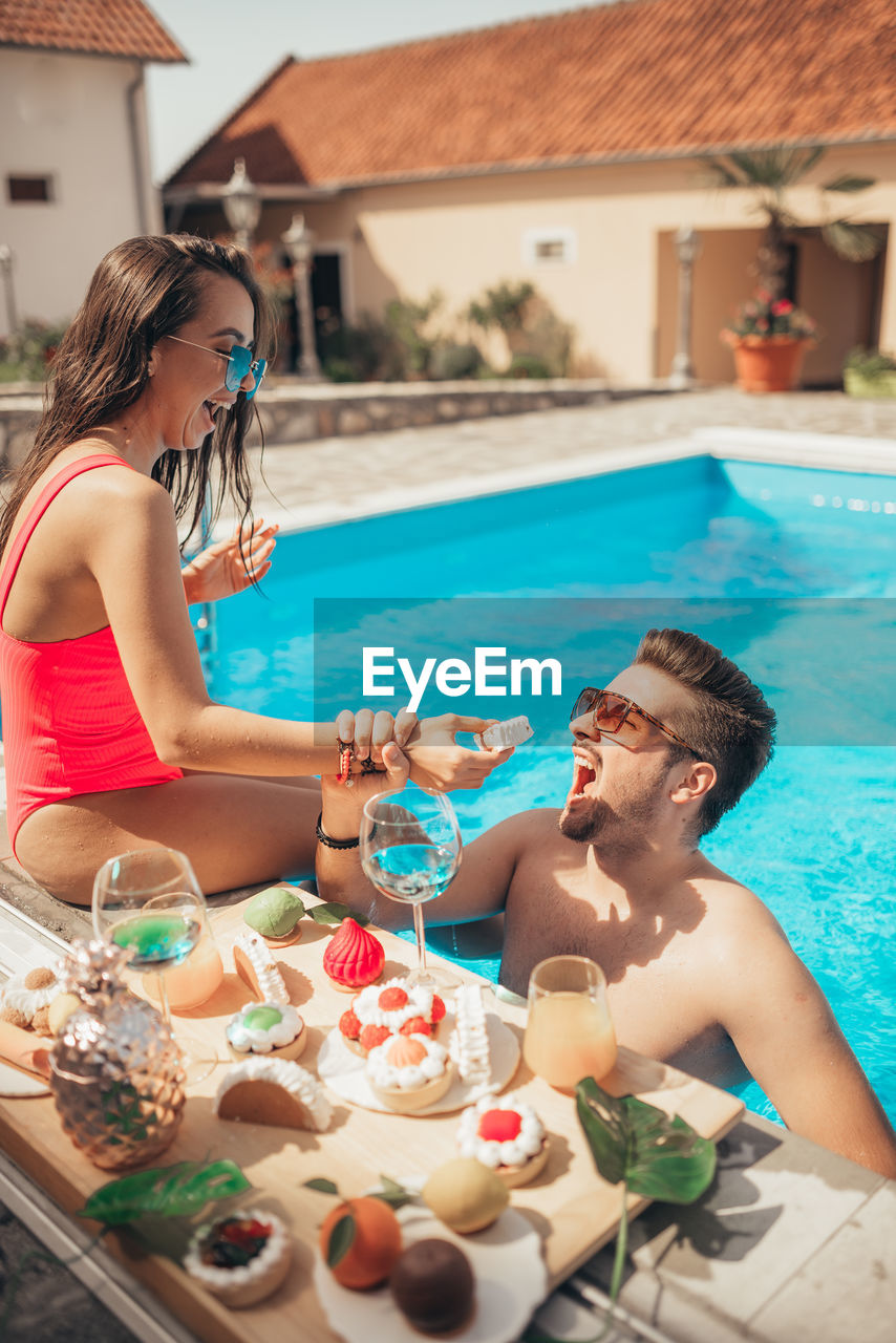 Young beautiful couple eating cookies by the pool. funny moments.