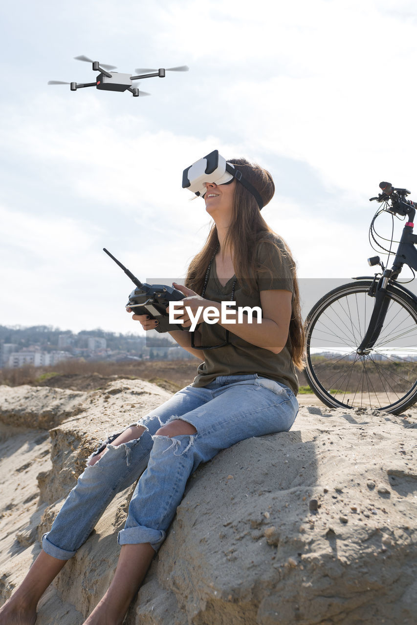 Young woman flying a drone with remote controller and virtual reality goggles