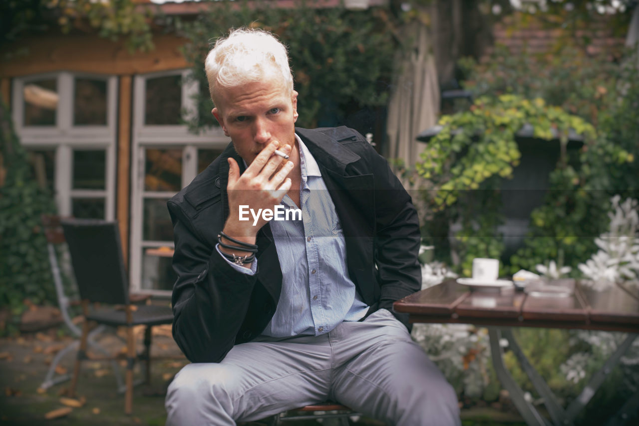 Portrait of man smoking cigarette sitting by table at cafe