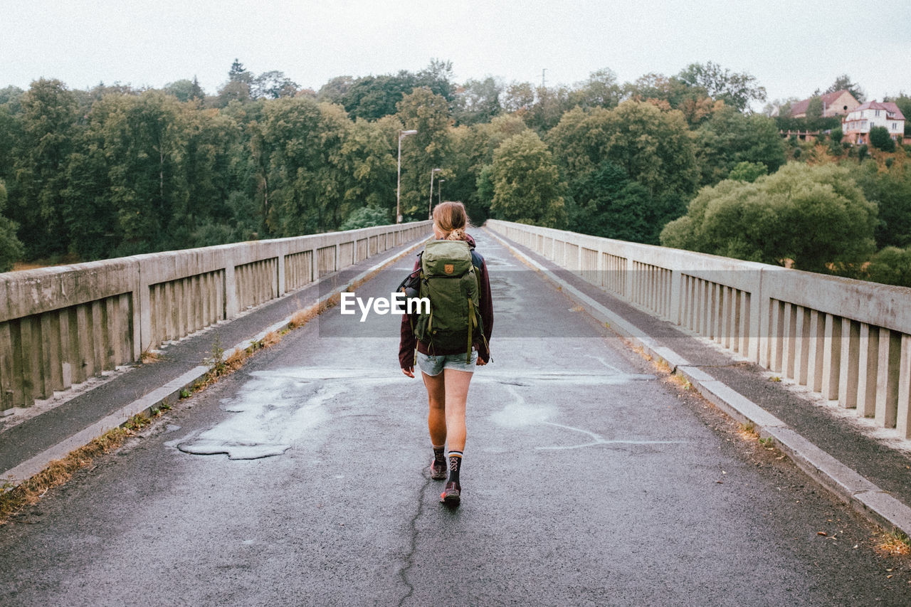 REAR VIEW OF MAN STANDING ON BRIDGE