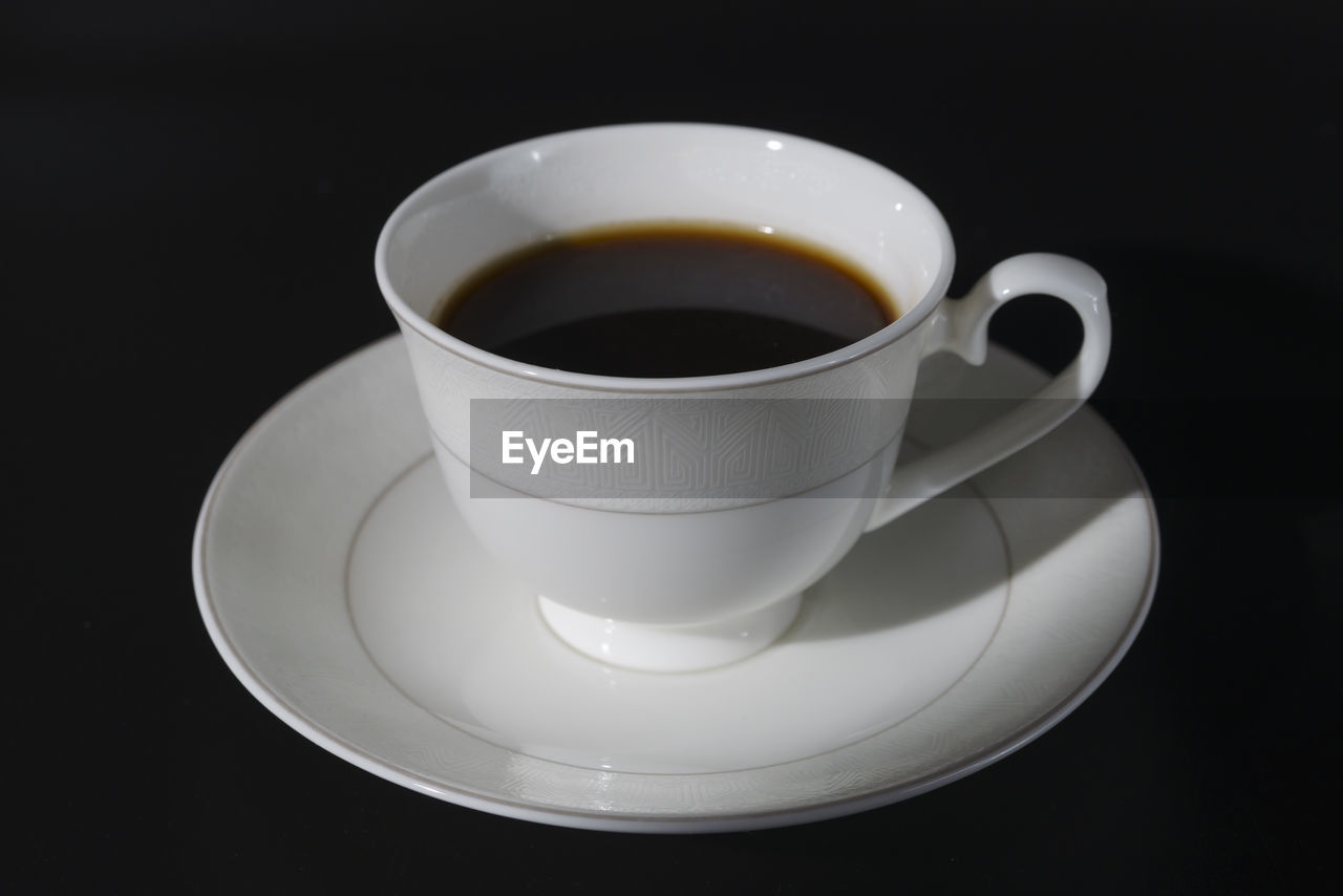 A black coffee poured into a porcelain coffee pair on a black background
