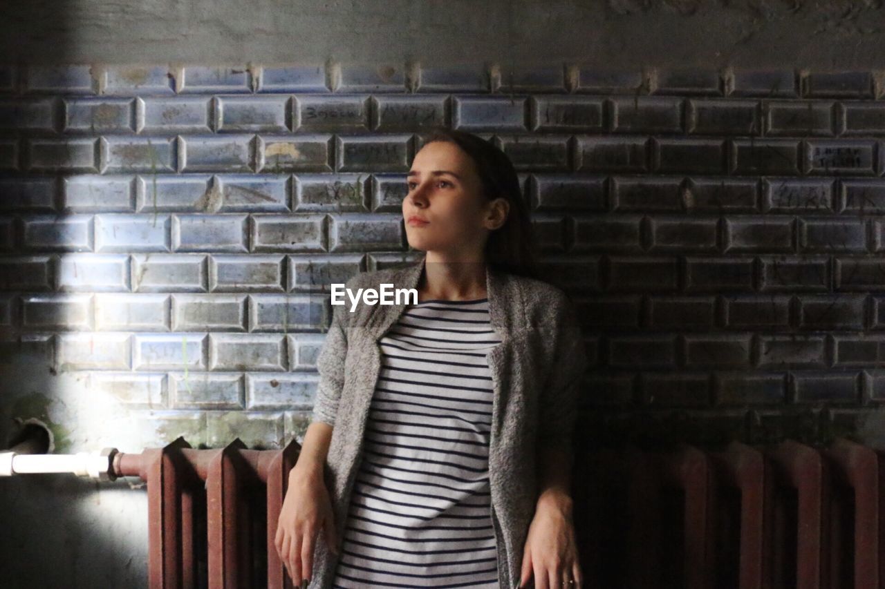 Young woman standing against brick wall