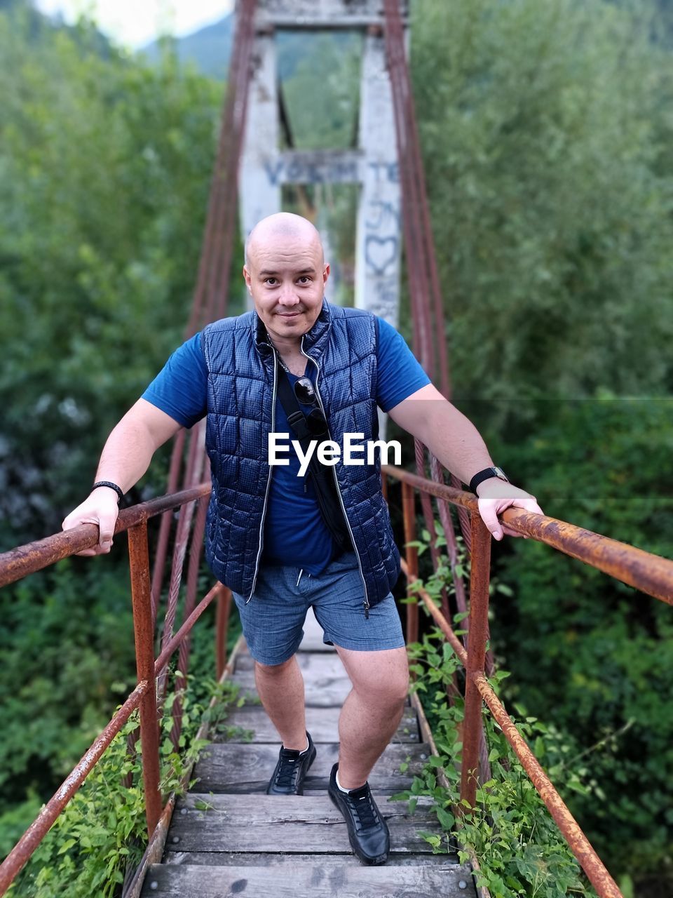 one person, adult, front view, full length, men, leisure activity, rope, casual clothing, rope bridge, nature, bridge, day, tree, adventure, portrait, lifestyles, plant, forest, looking at camera, outdoors, smiling, mature adult, standing, emotion, balance, sports, happiness, activity, architecture, senior adult, person, vitality, holding, safety harness, canopy walkway, clothing, strength, footbridge, motion, land