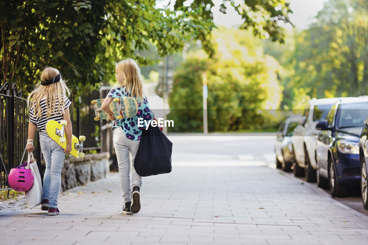 Rear view of girls with skateboards walking on cobbled street