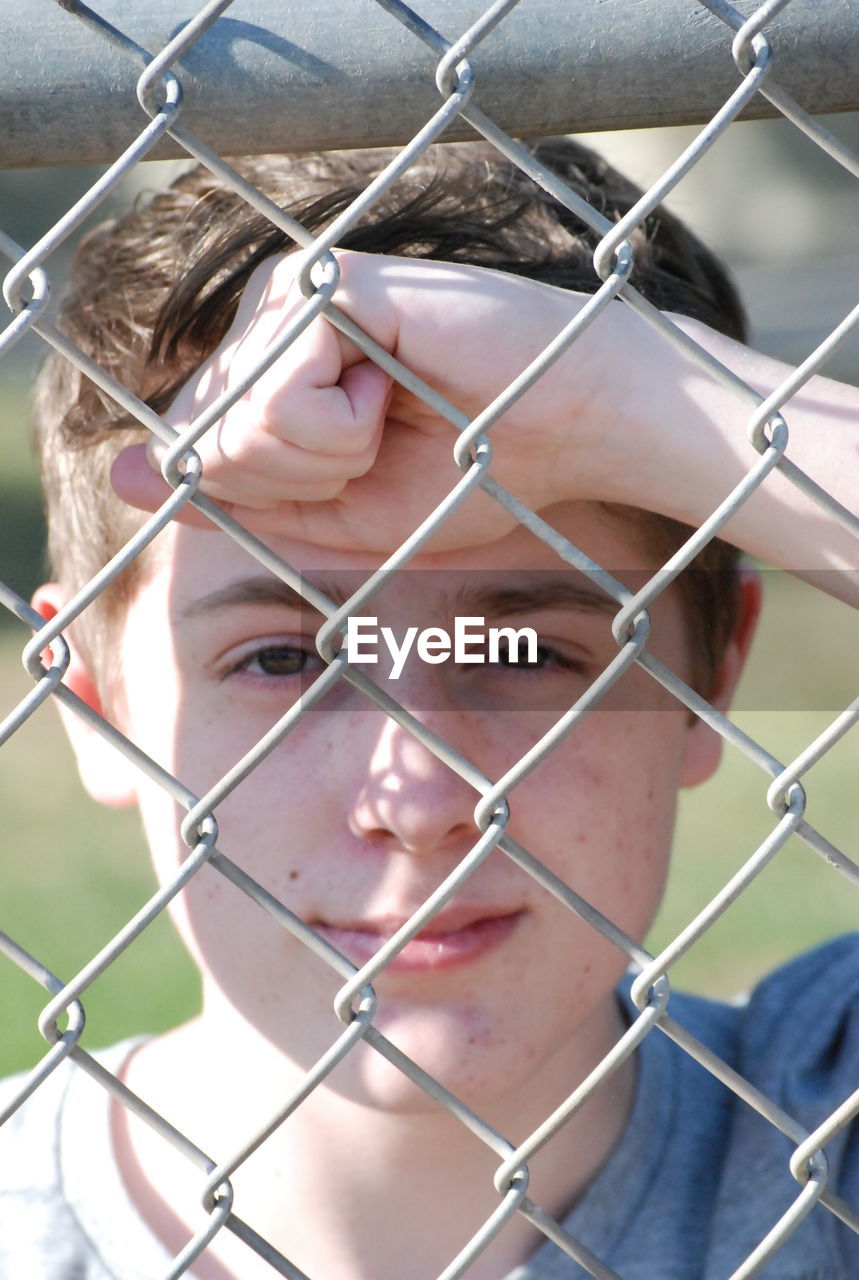 Portrait of young man seen through chainlink fence