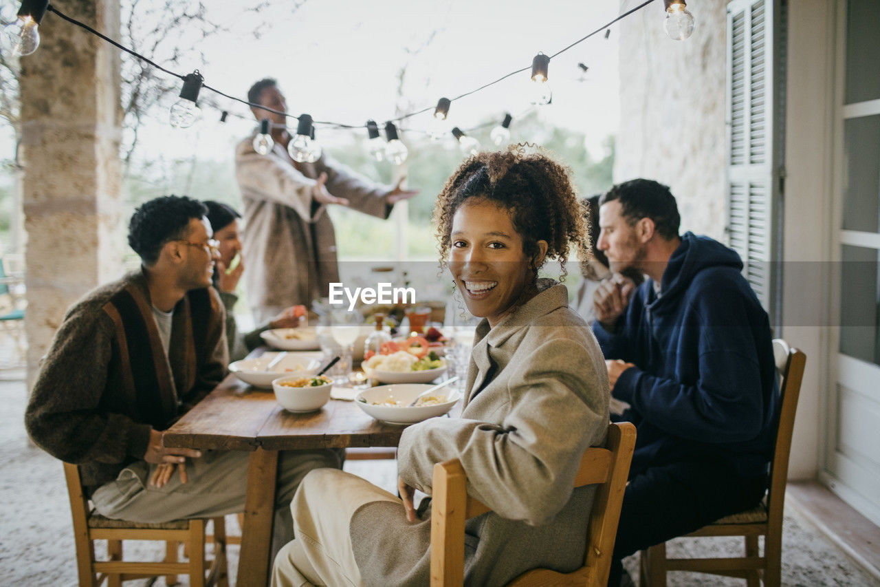 Portrait of happy young woman sitting at dining table with friends during dinner party