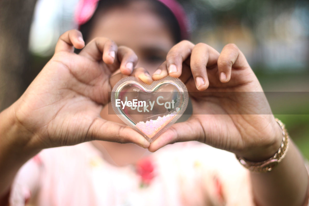 Close-up of girl holding heart shape with text