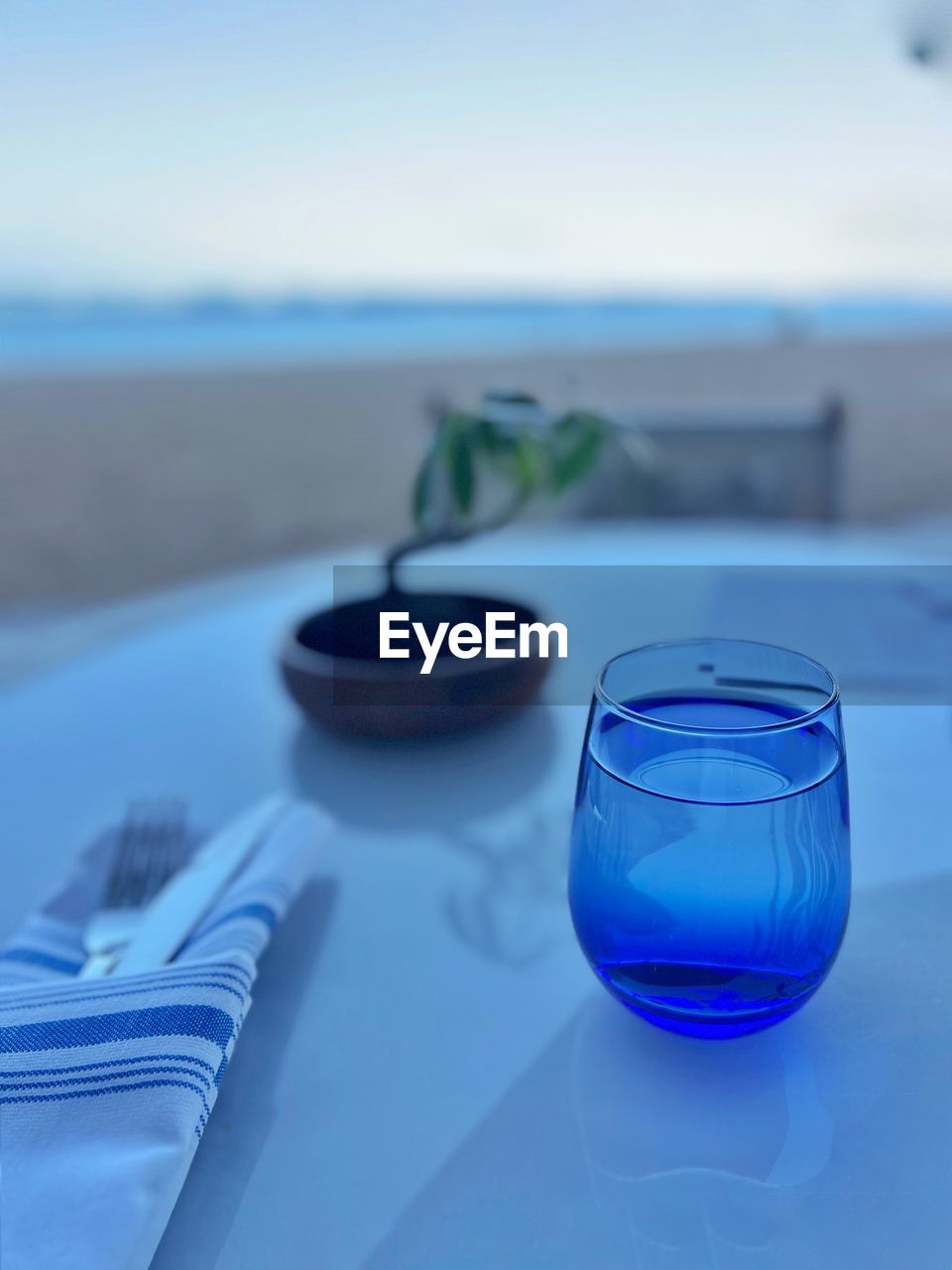 blue, water, household equipment, glass, drinking glass, nature, food and drink, no people, drink, sky, focus on foreground, sea, refreshment, land, table, cobalt blue, wine glass, azure, outdoors, close-up, beach, food, alcohol, day, freshness
