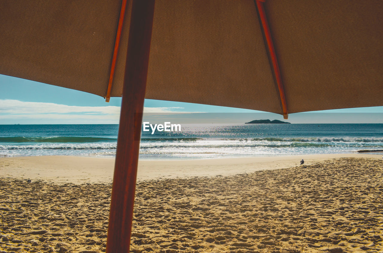 BEACH UMBRELLA BY SEA AGAINST SKY