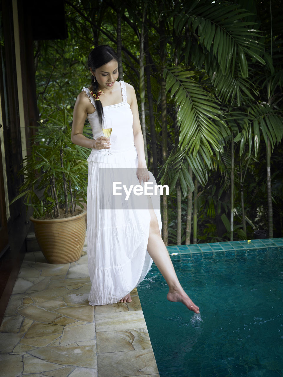 Young woman holding champagne flute while standing at poolside