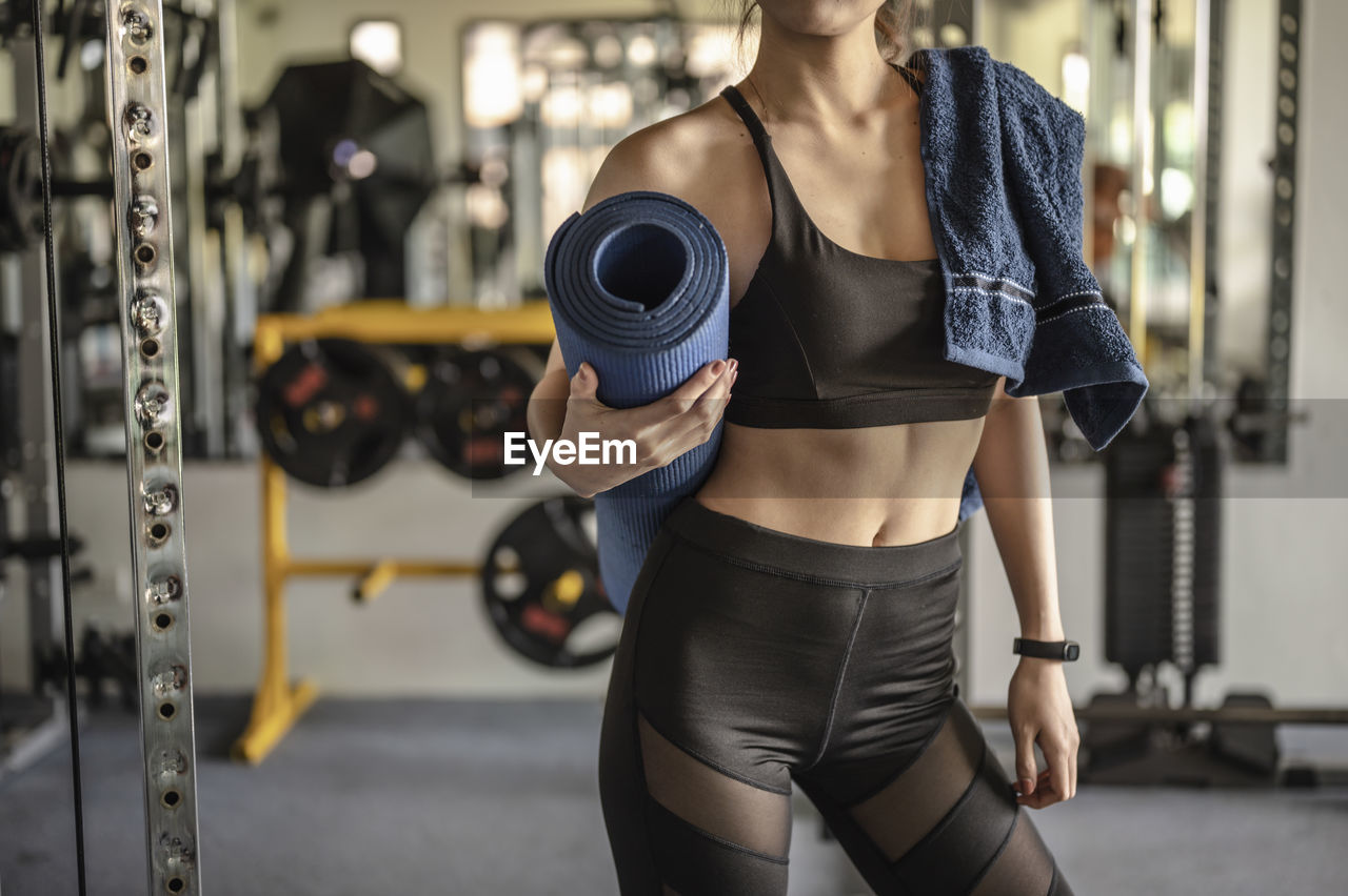 Midsection of woman holding mat while standing in gym
