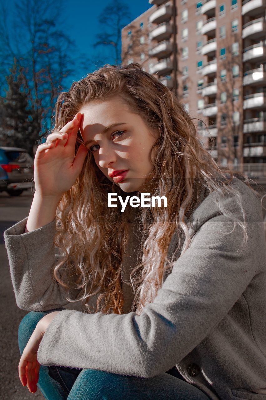 Portrait of beautiful young woman shielding eyes while sitting outdoors