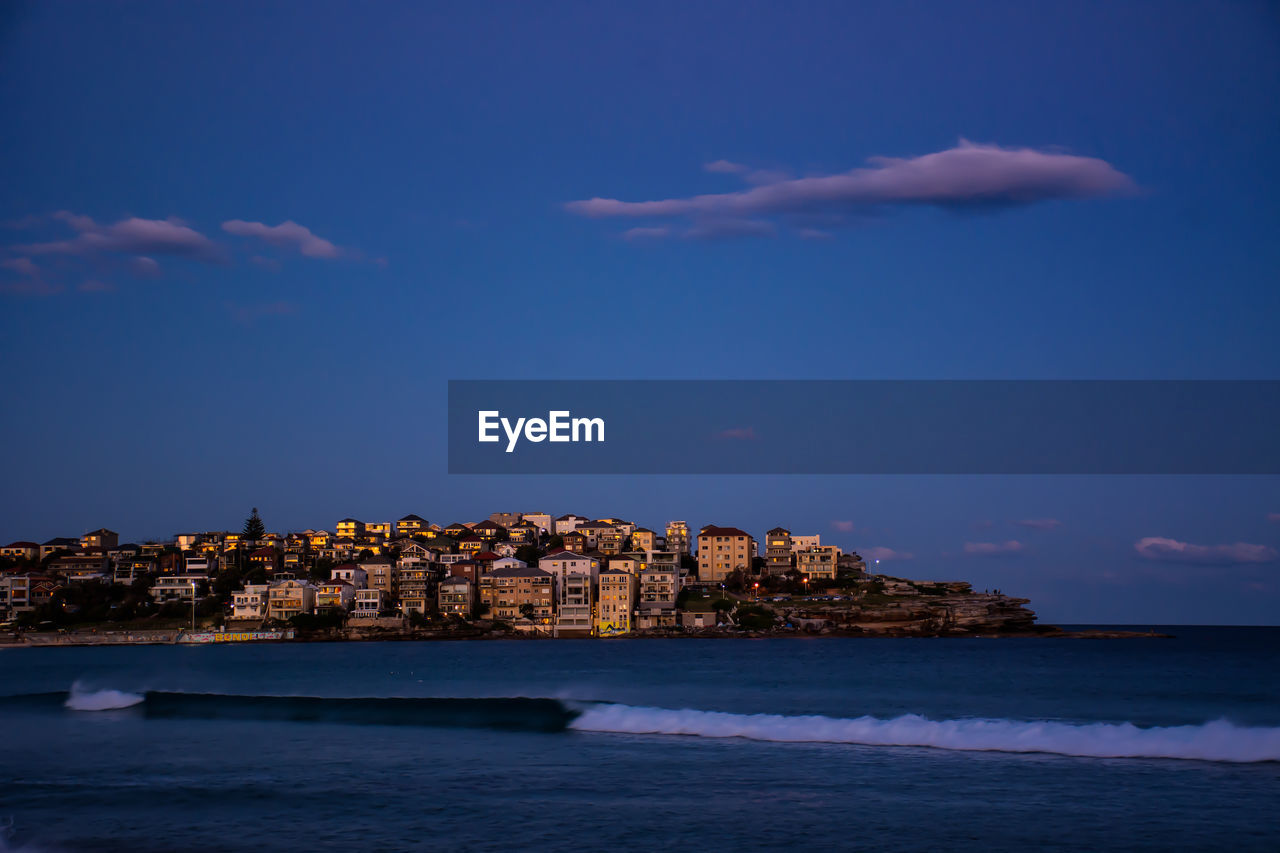 Sea by buildings against sky during sunset