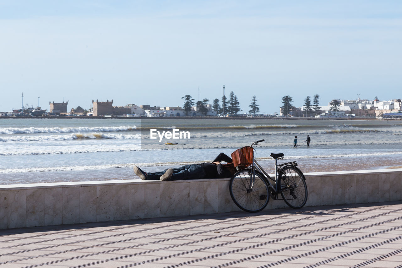 Man with bicycle lying on retaining wall against