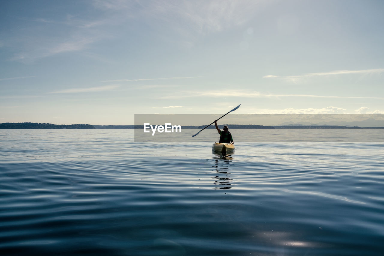 Silhouette man kayaking in sea against sky