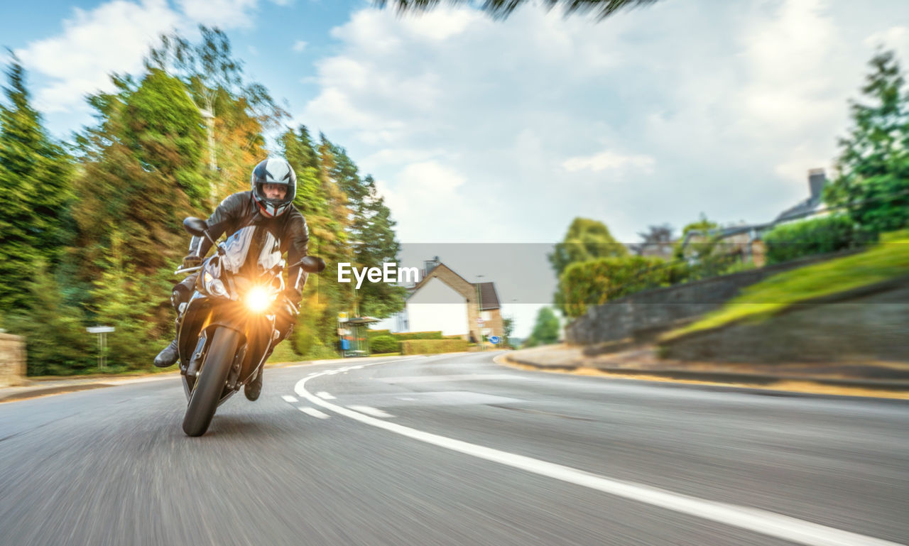 Blurred motion of man riding motorcycle on road against cloudy sky