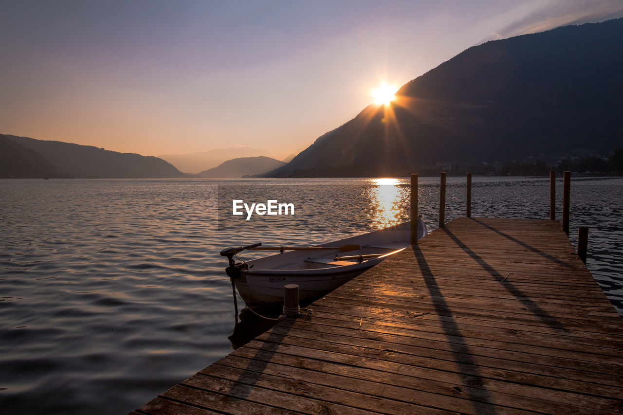 Boat moored by jetty in lake against sky during sunset