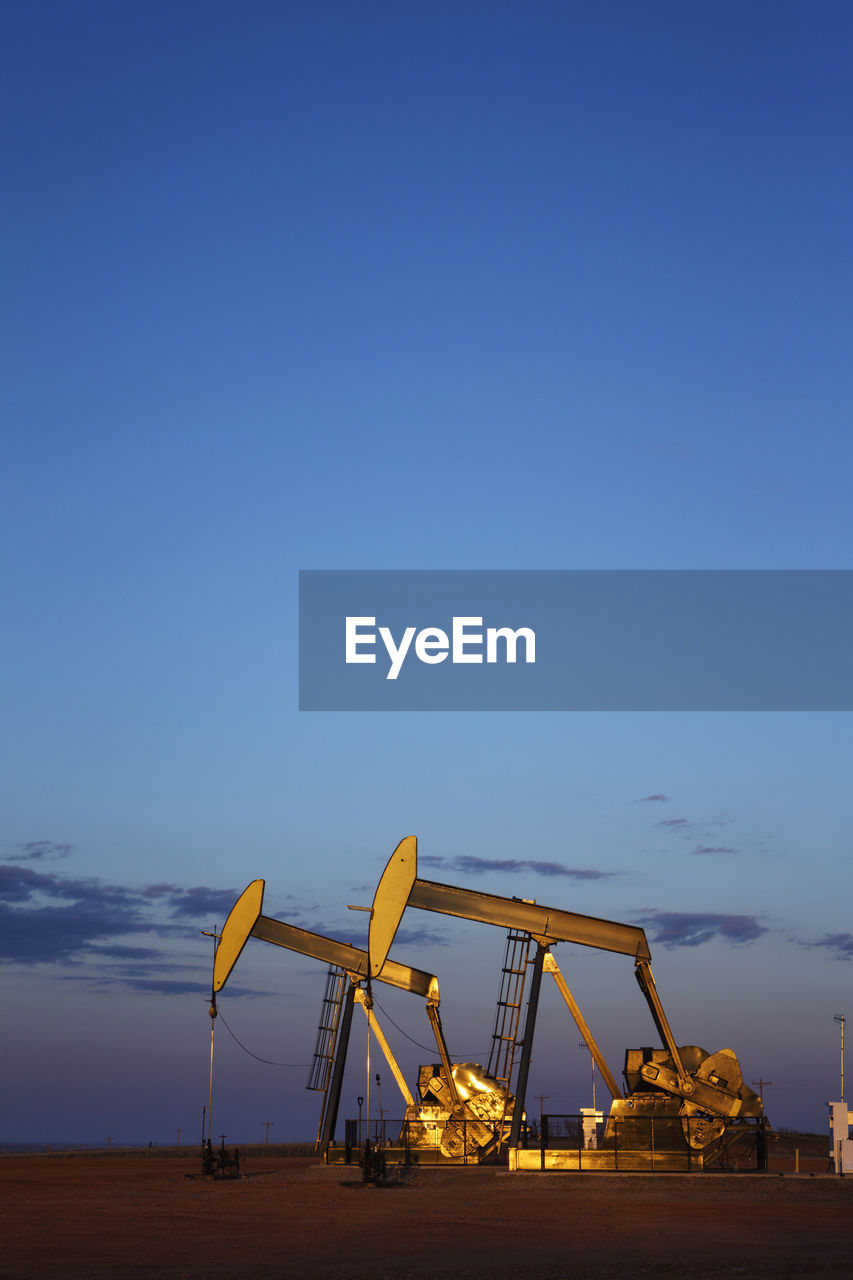 Oil pumps on field against blue sky during dusk