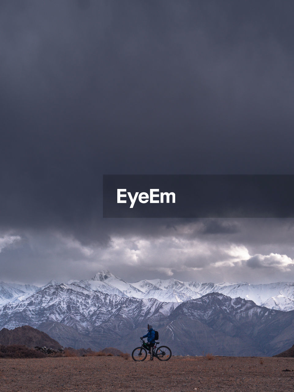 Man with bicycle against mountains and stormy clouds during winter