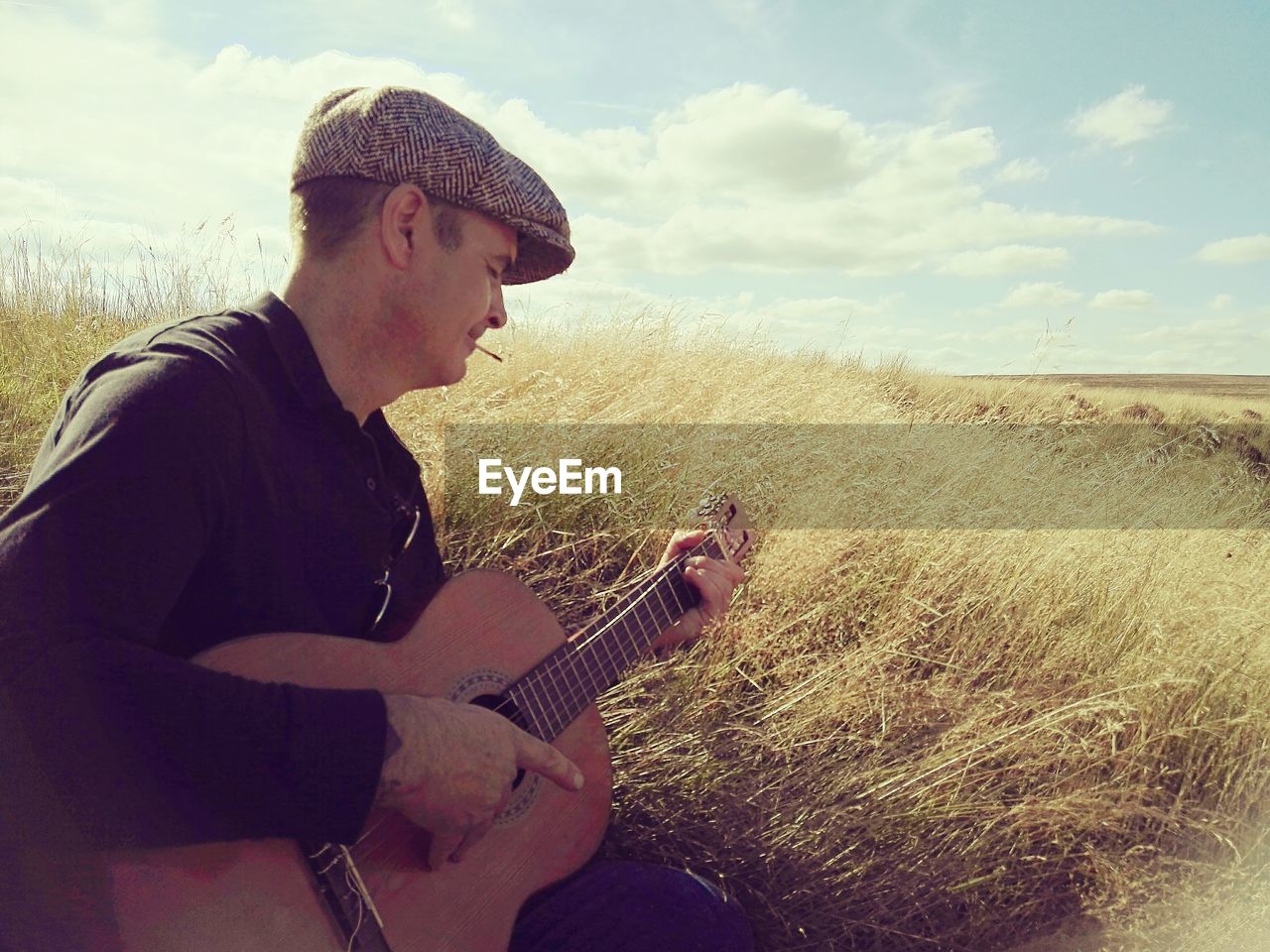 Man playing acoustic guitar on grassy field against sky