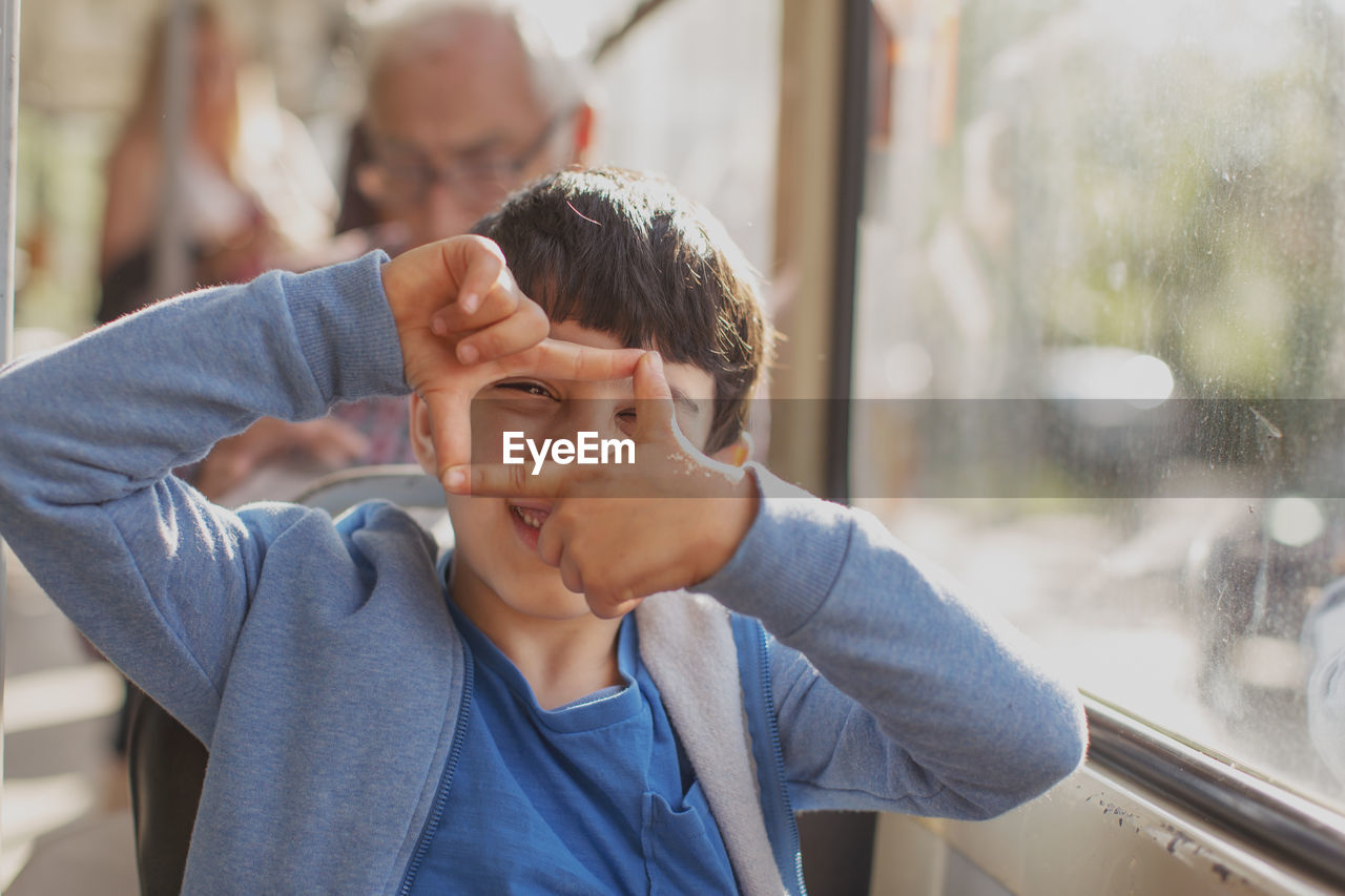 Portrait of boy looking through finger frame in bus