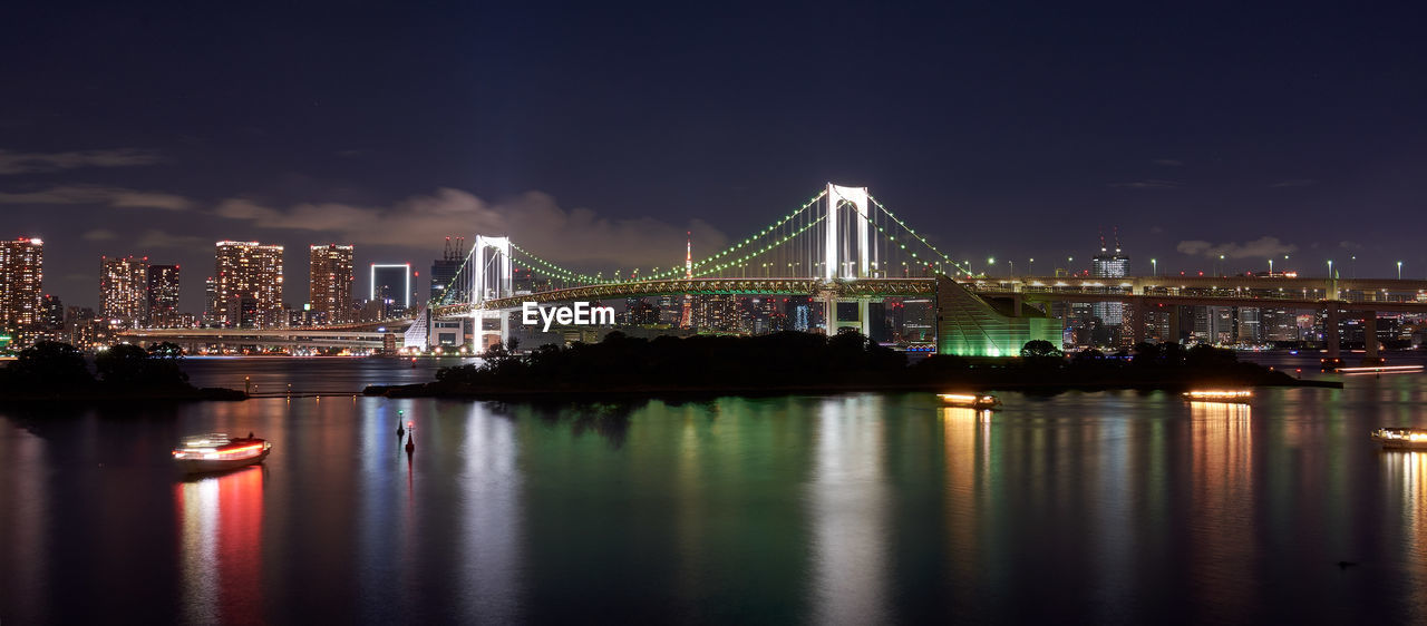 Illuminated bridge over river in city against sky at night