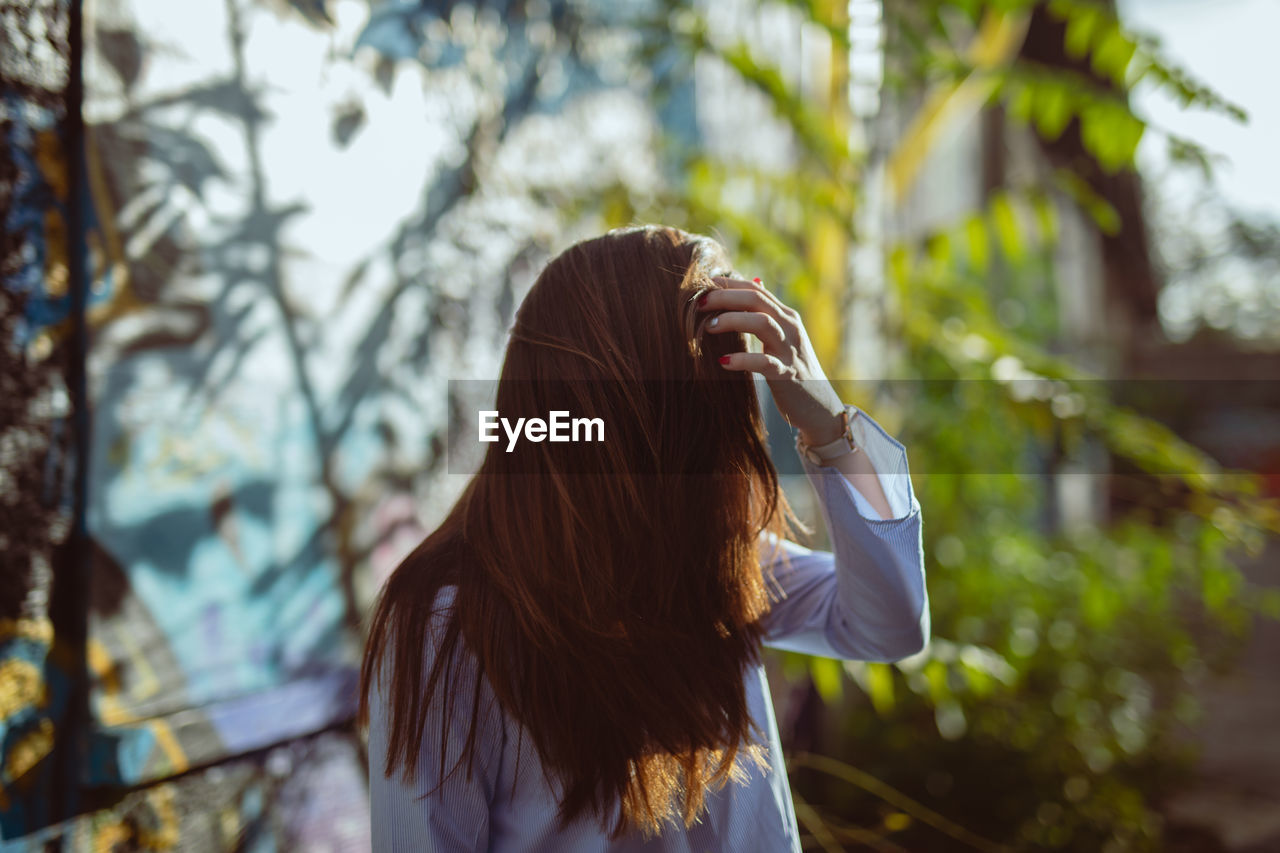 Young woman with tousled hair standing against plants