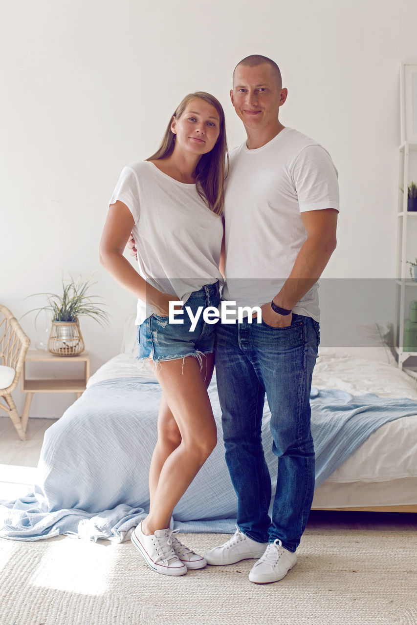 Couple in white t-shirts and blue jeans stand in a white room