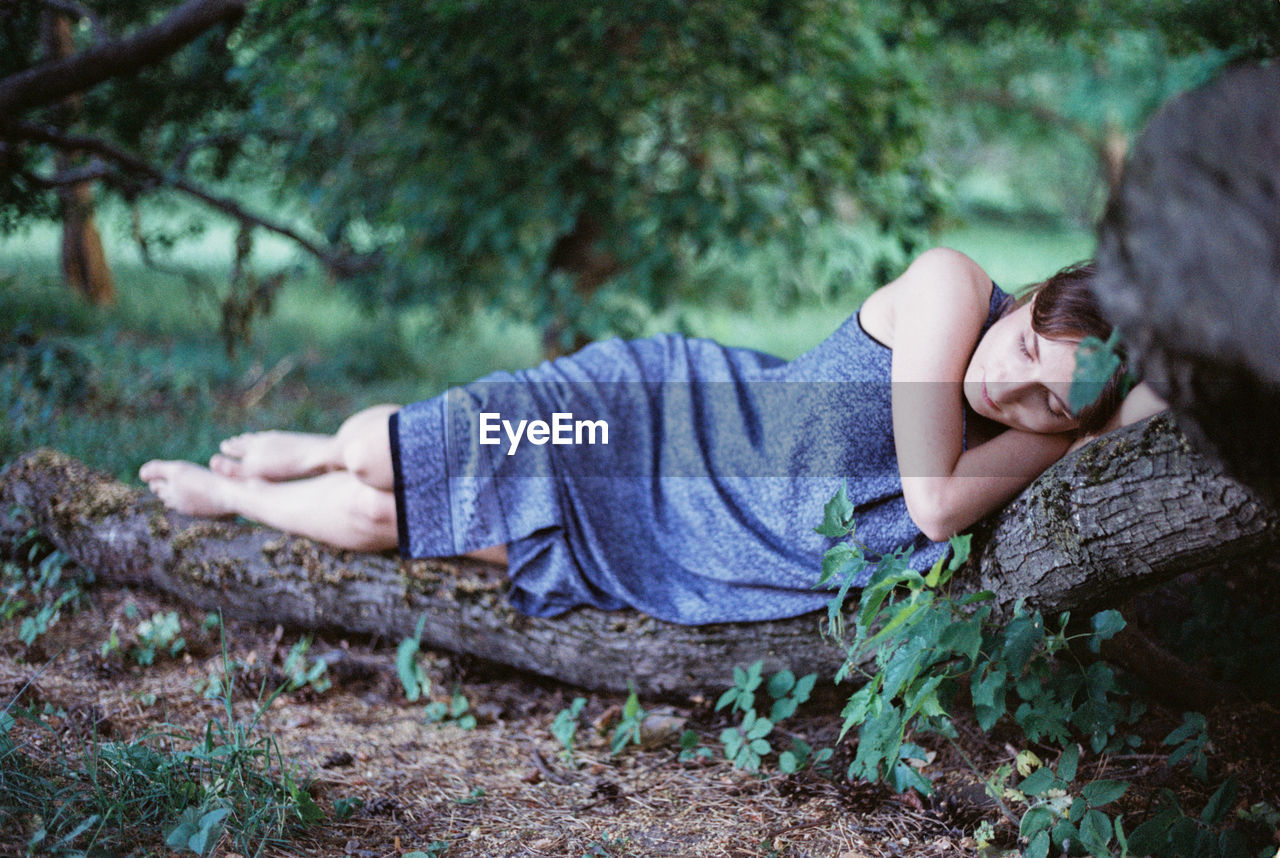 Woman sleeping on log in forest