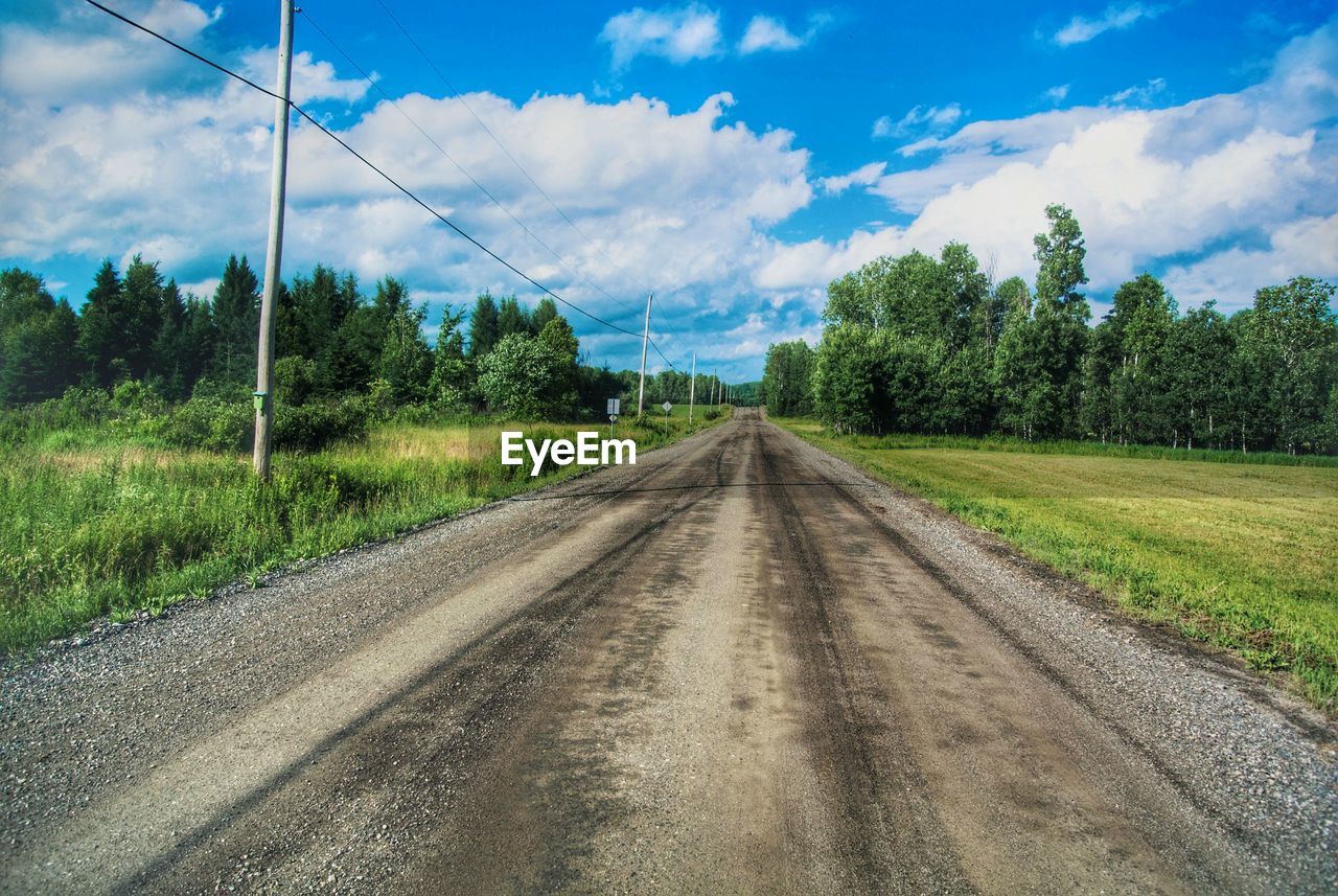 Empty road amidst field against cloudy sky