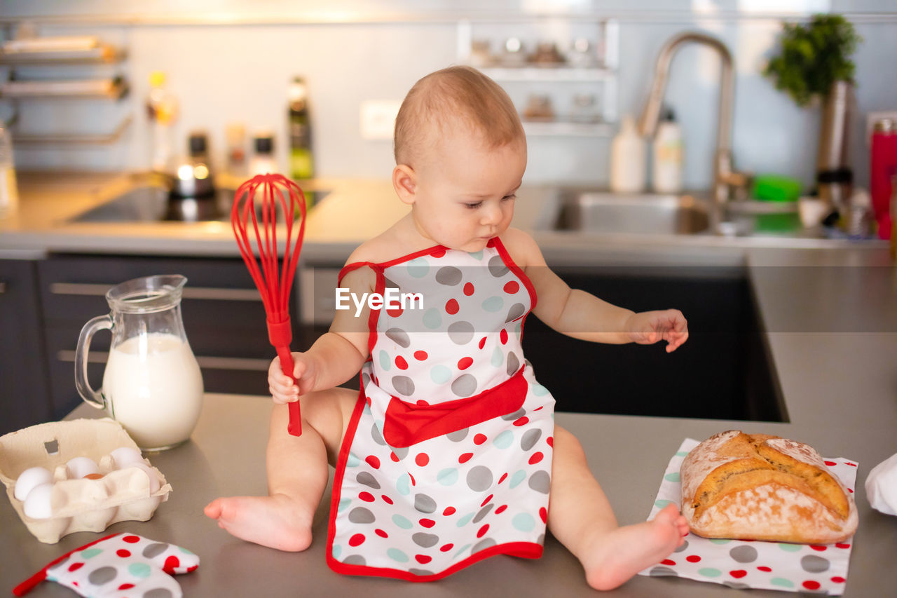 Full length of cute girl holding wire whisk at home