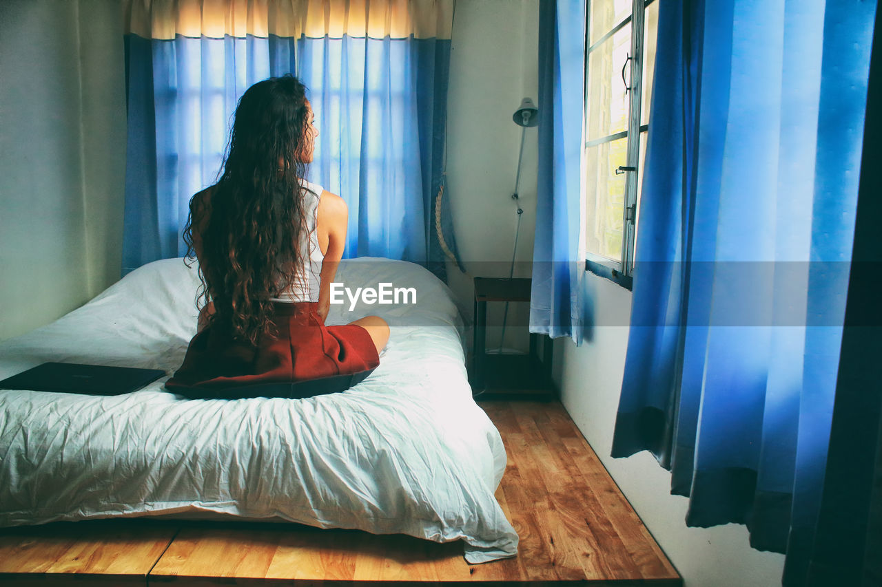 Rear view of woman sitting on bed