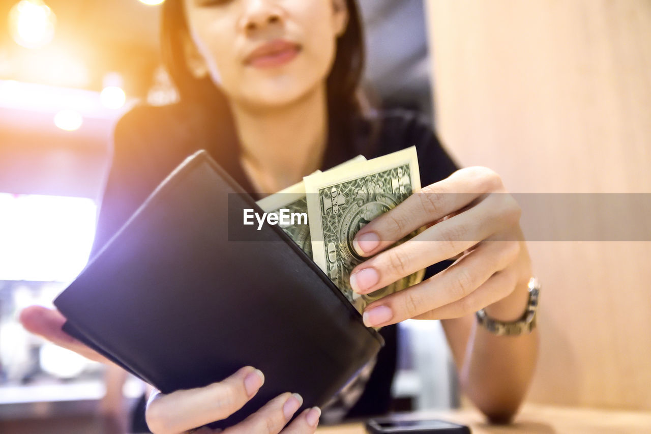 Close-up of woman putting paper currency in wallet at table