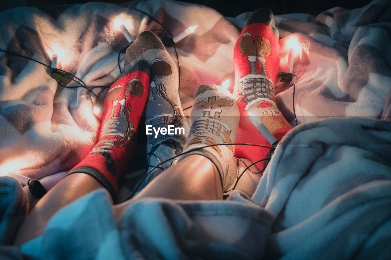 Low section of people wearing socks with illuminated string lights sitting on bed