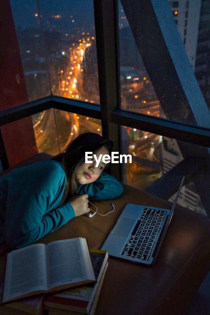 Young woman using laptop while lying by window at home