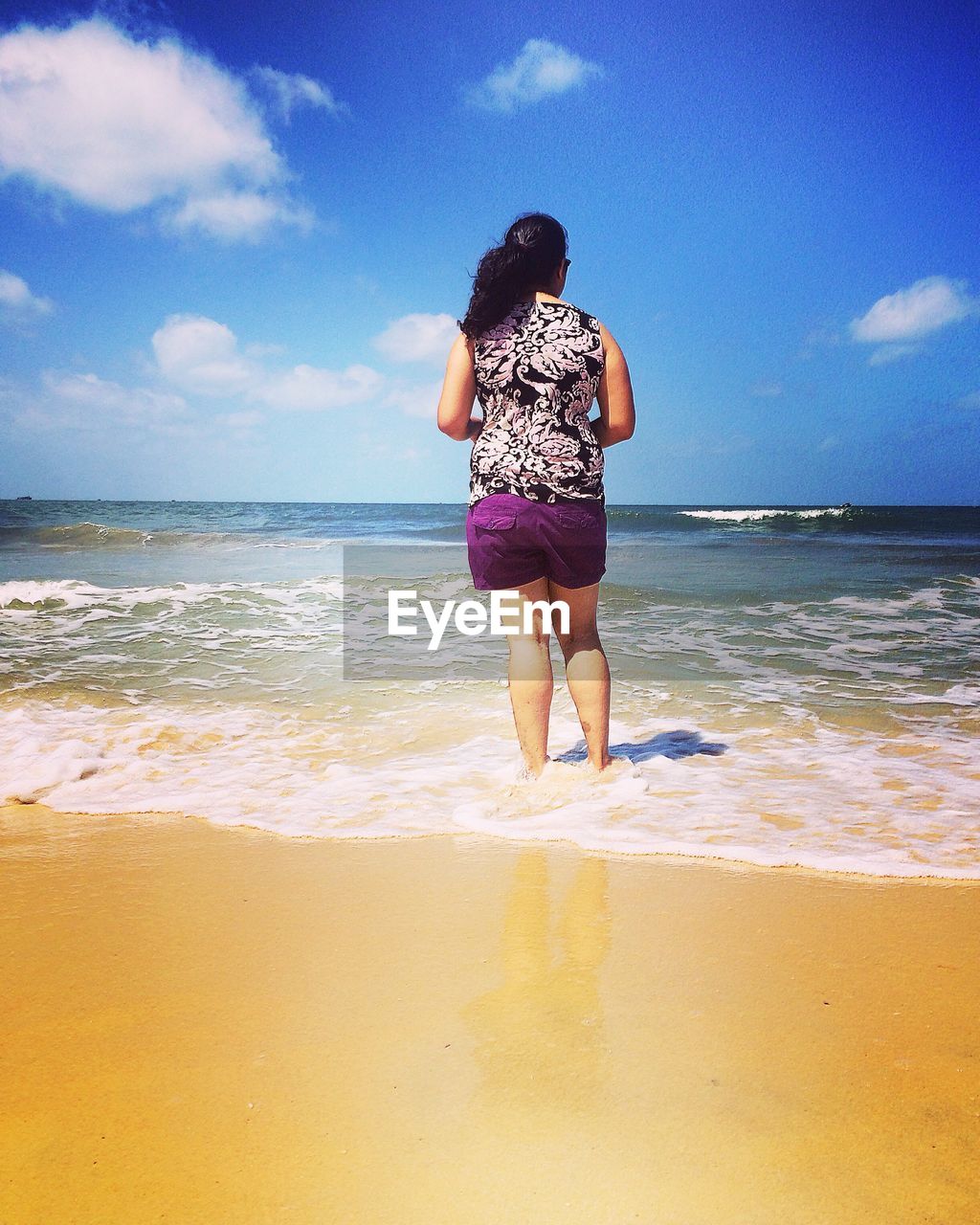 Rear view of woman standing on shore at beach against sky