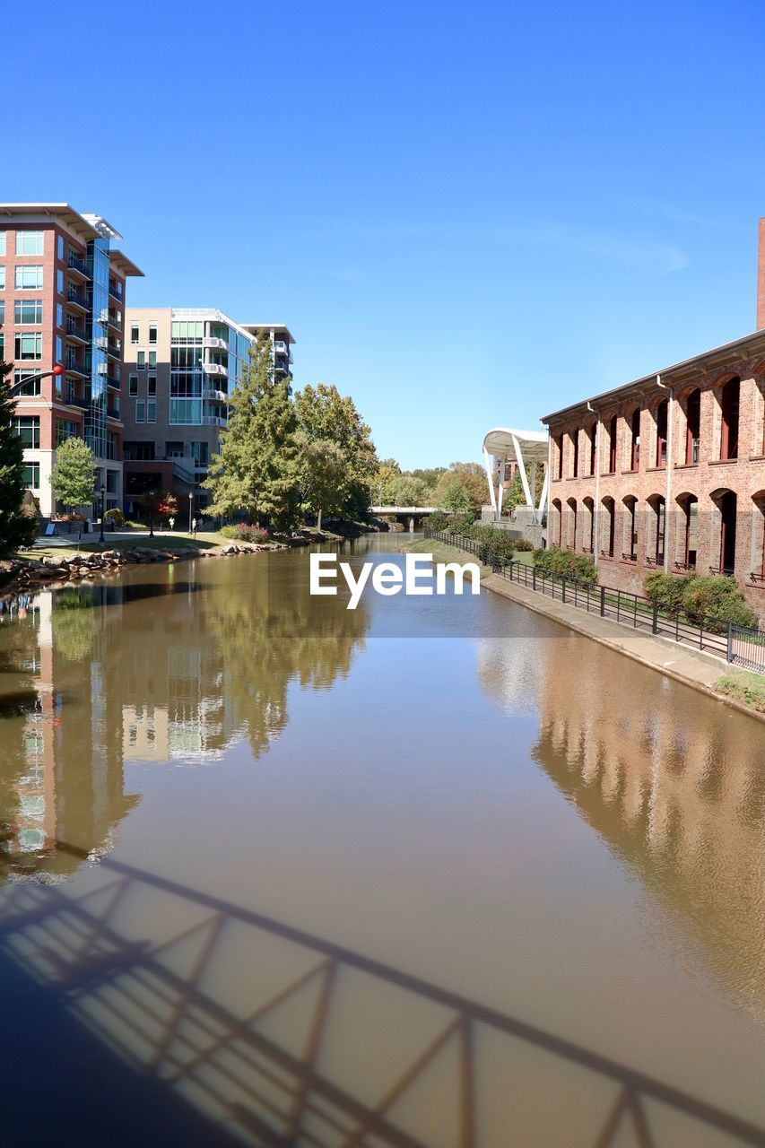 Reflection of buildings in river against clear blue sky