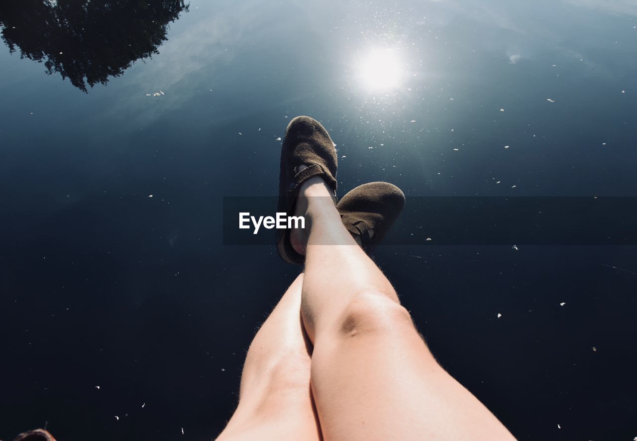 High angle view of woman legs over calm lake during sunny day