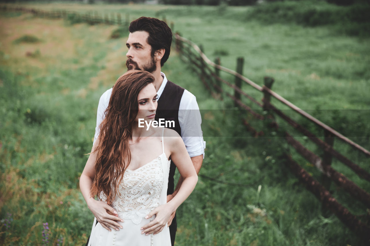 Wedding couple looking away while standing on field