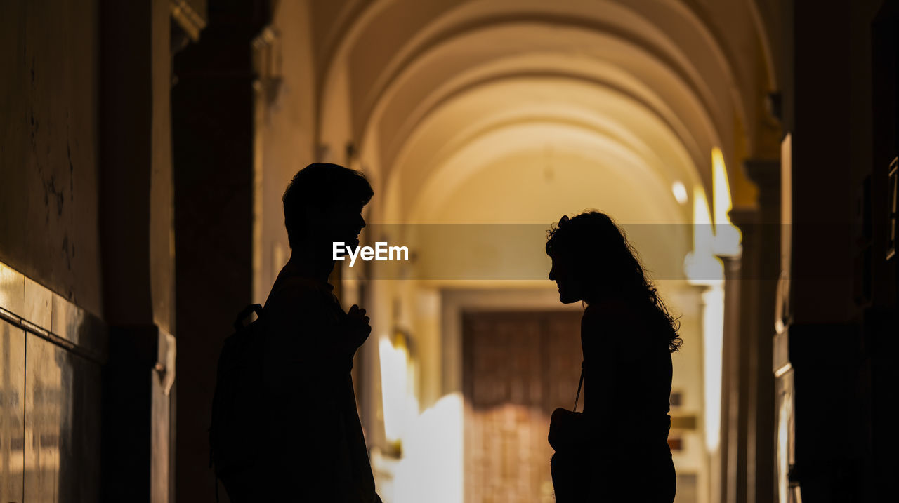 Silhouette of two young people chatting on building corridor with sunlight and shadow