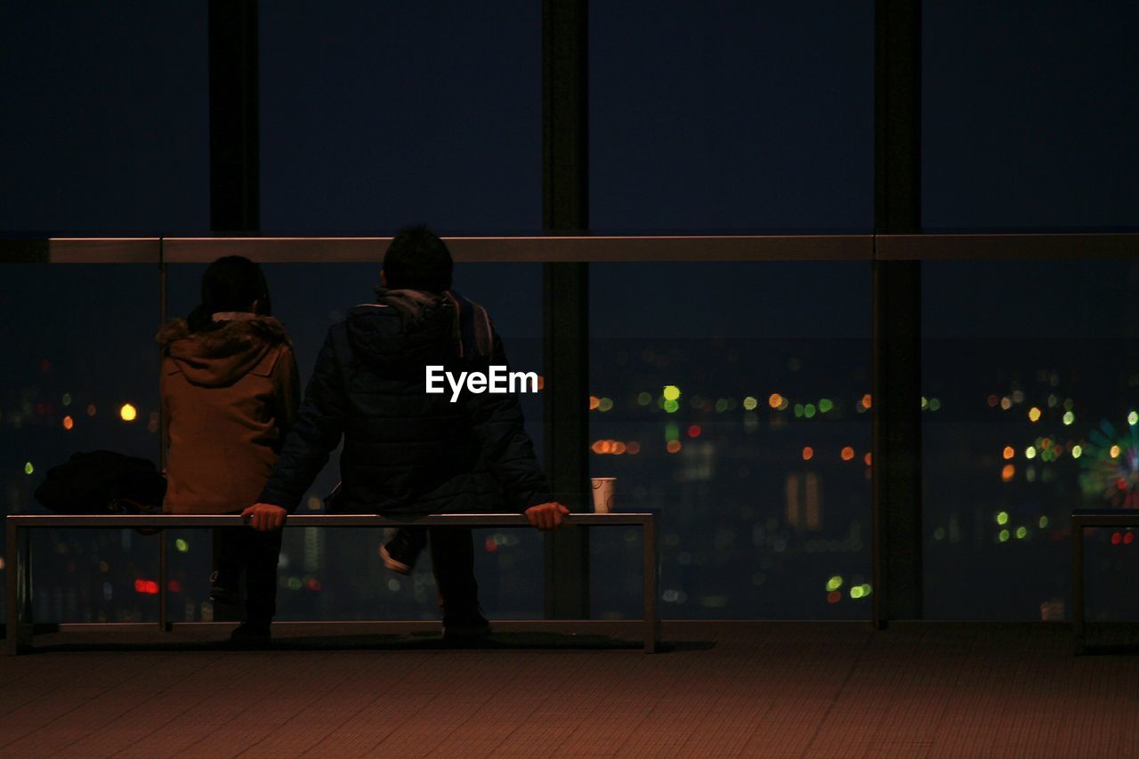 Rear view of couple sitting on bench at promenade during night