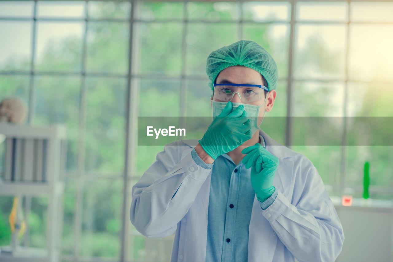 Portrait of scientist wearing surgical mask and cap standing in laboratory