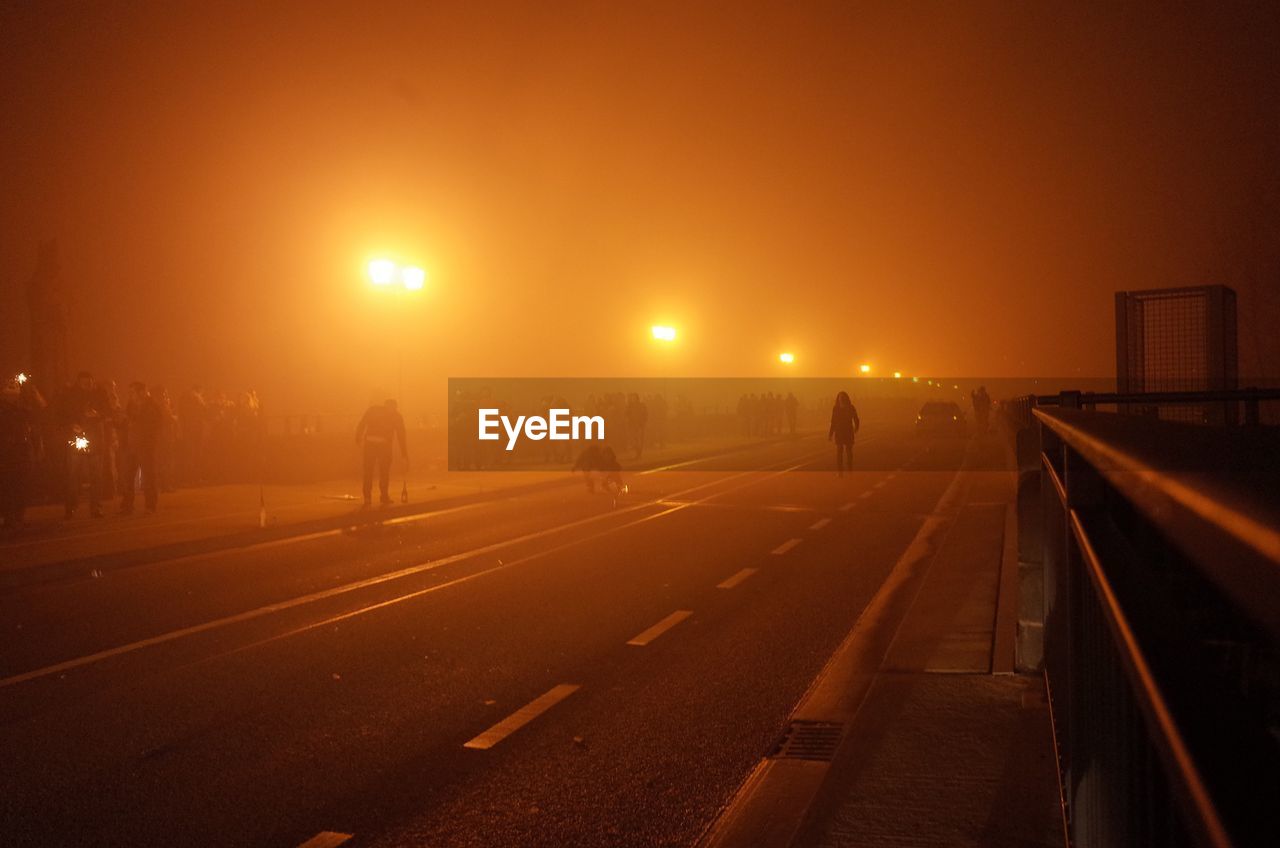 Illuminated road against sky during foggy weather at night