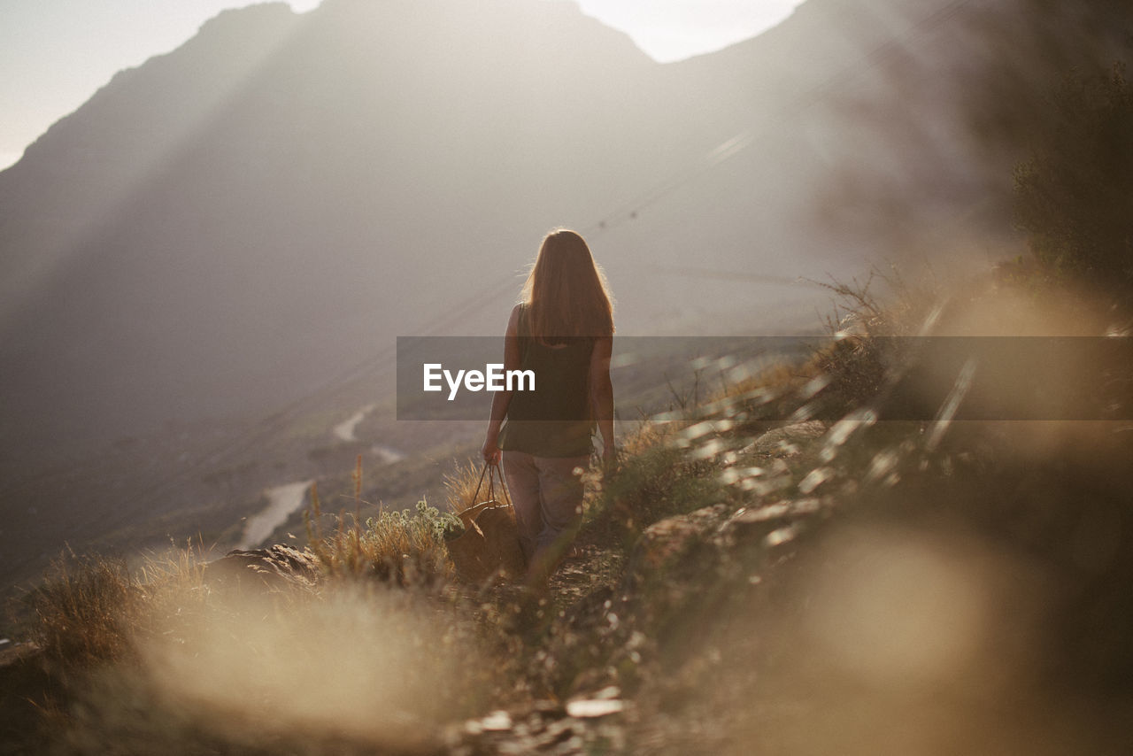 REAR VIEW OF WOMAN WALKING ON MOUNTAIN DURING RAINY DAY