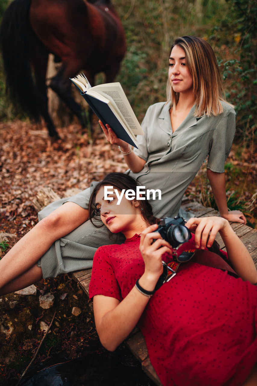 Woman reading book with friend in forest