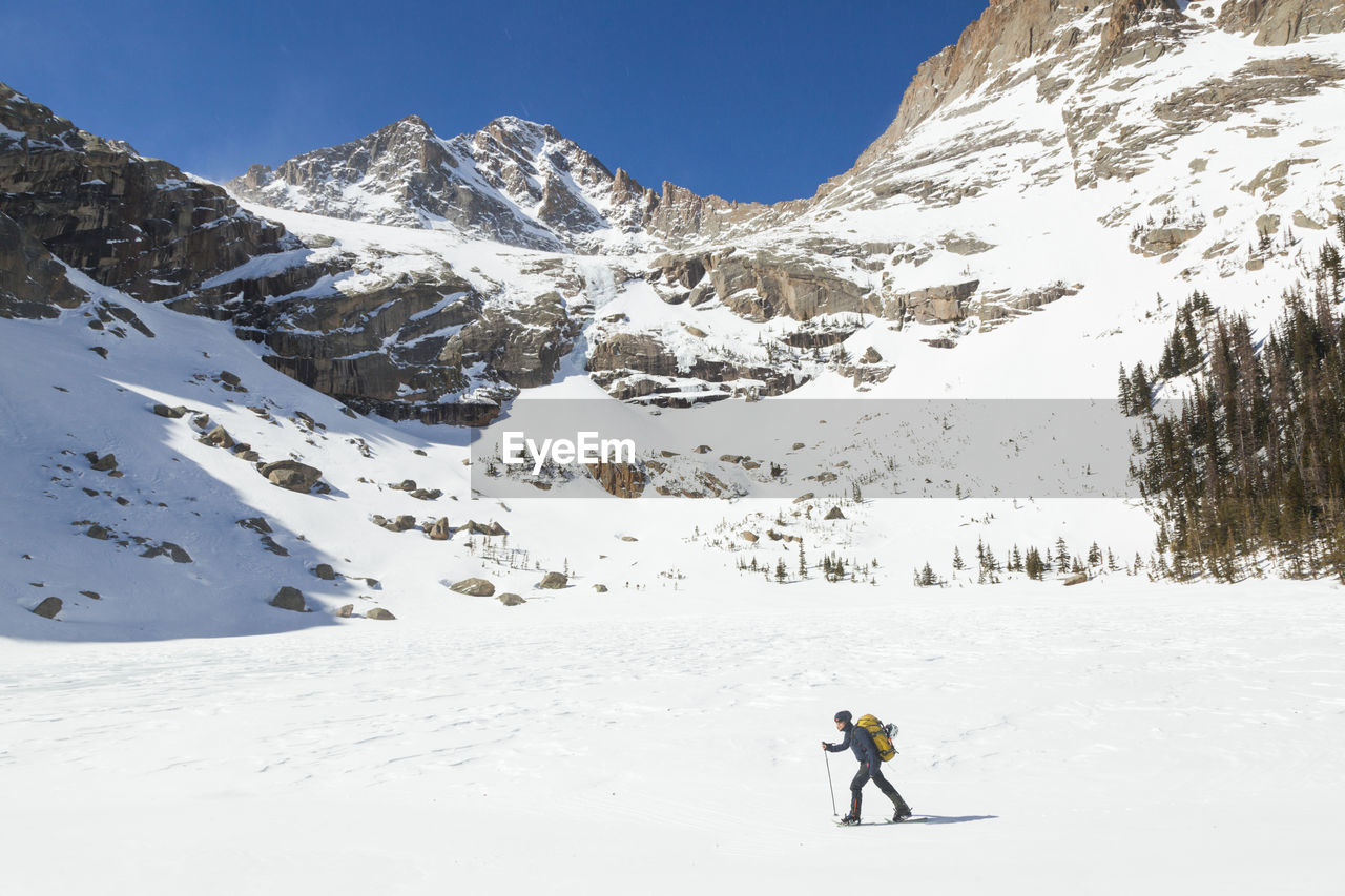 Woman hikes across frozen black lake, rocky mountain national park